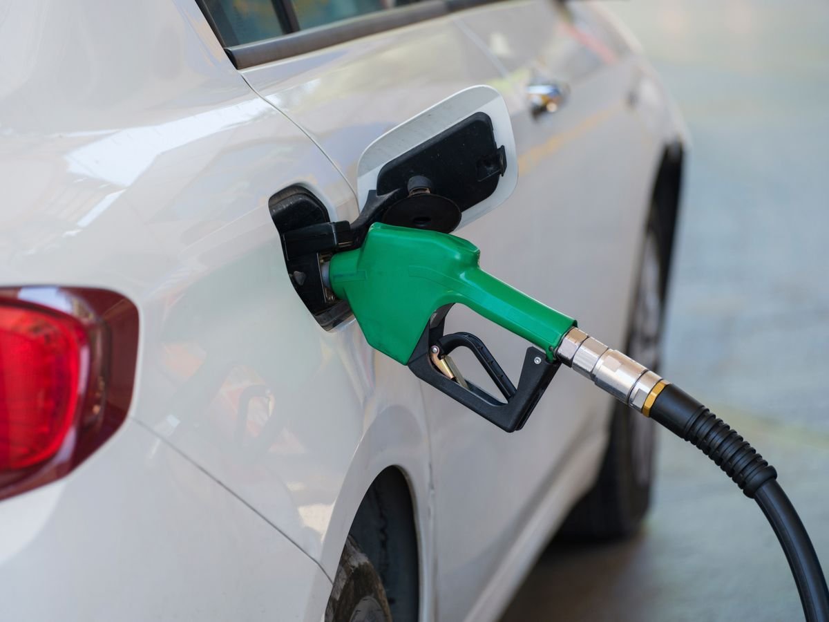 A fuel nozzle refuelling a white car at a gas station pump
