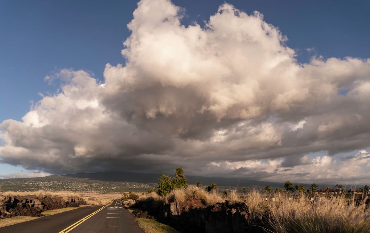 A wide highway running toward mountains under dramatic clouds near Hilo on Hawaii's Big Island