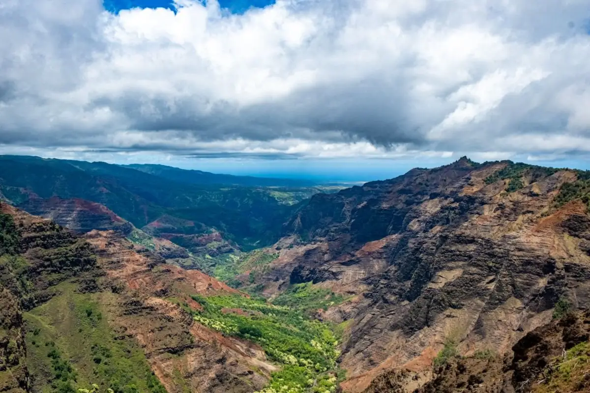 Waimea Canyon on Kauai, Hawaii, with red cliffs and green ridges under a cloudy sky