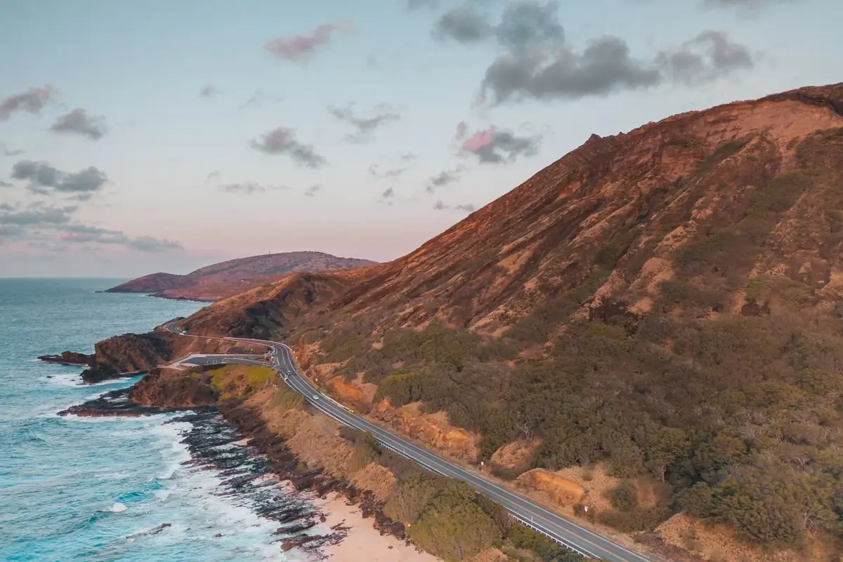 A narrow coastal road running along rugged cliffs above the ocean in Hawaii