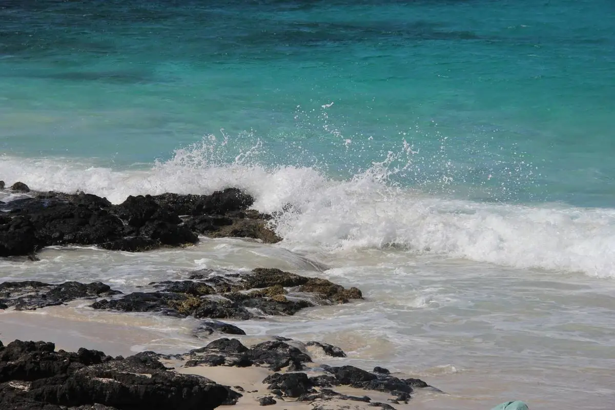 Waves breaking on dark lava rock and white sand on the Kailua-Kona coast