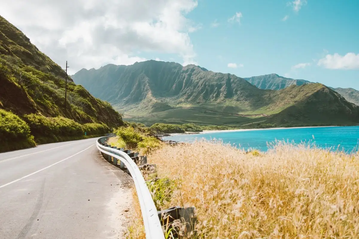 A coastal road curving between green Hawaiian mountains and blue ocean
